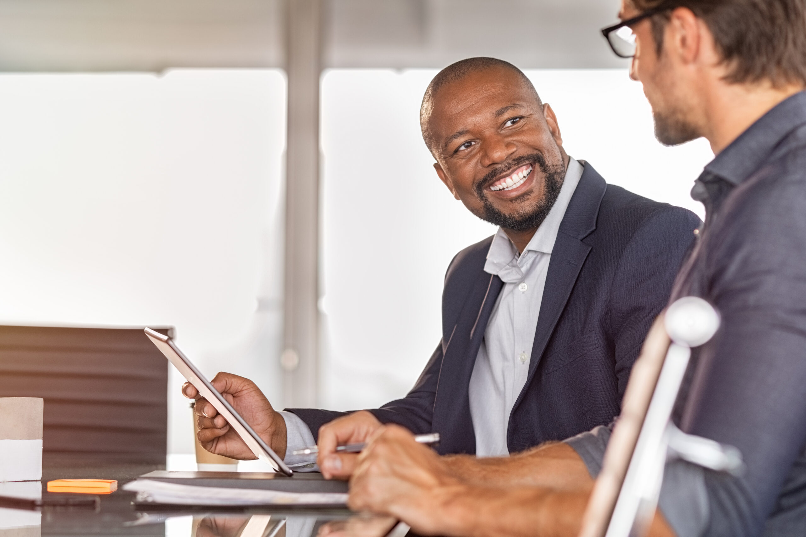 Business partners working on project together. Smiling african businessman working and discussing with employee in modern office over a report. Happy and successful leader with colleague in conference room discussing new project.