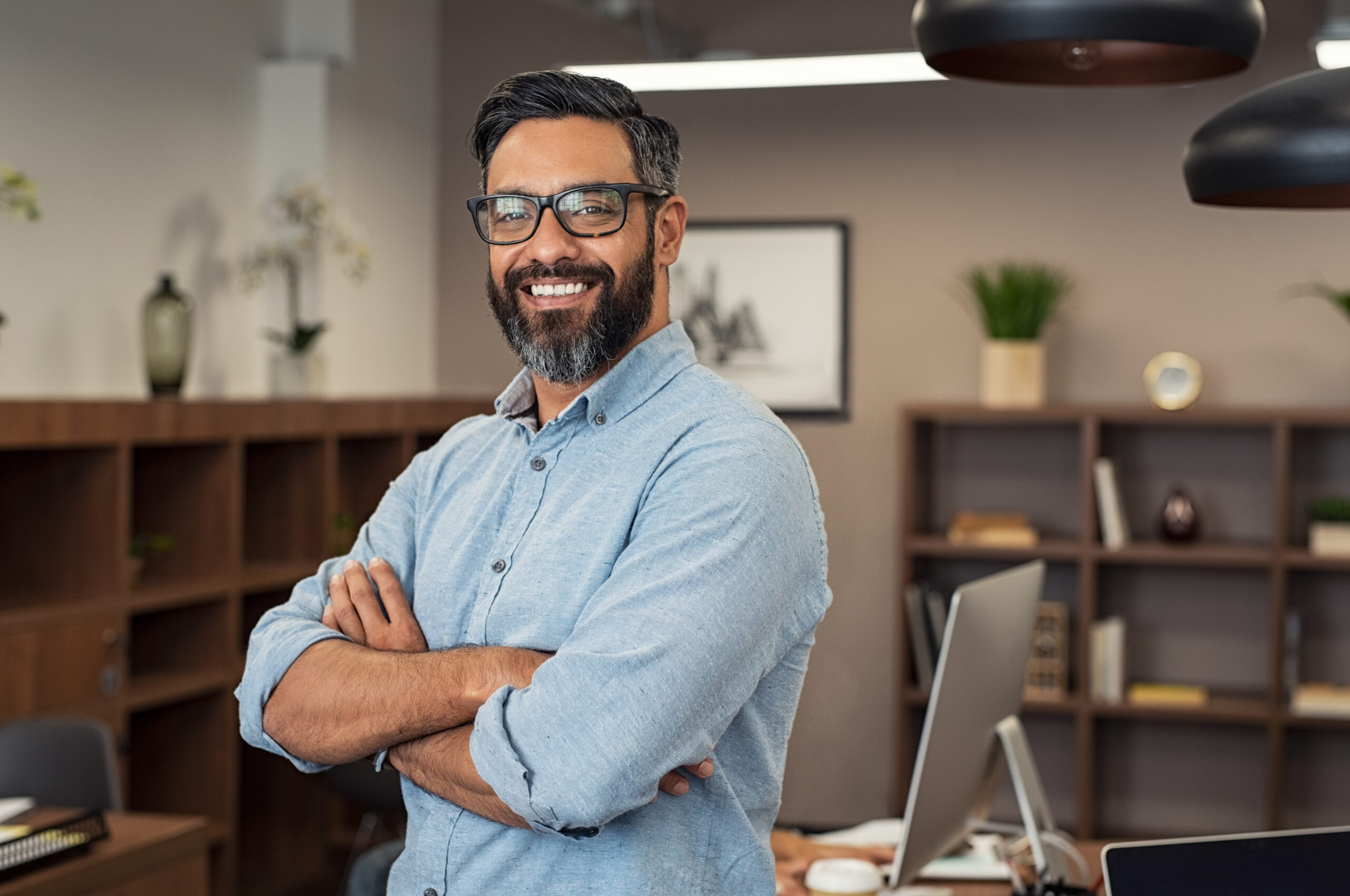 Portrait of happy mature businessman wearing spectacles and looking at camera. Multiethnic satisfied man with beard and eyeglasses feeling confident at office. Successful middle eastern business man smiling in a creative office.